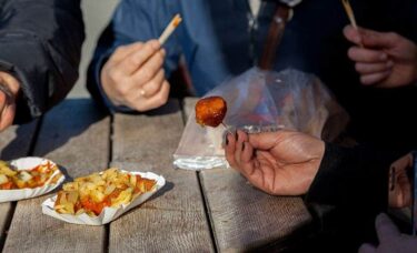 Two people eating curry wurst with fries, sitting next to wooden table